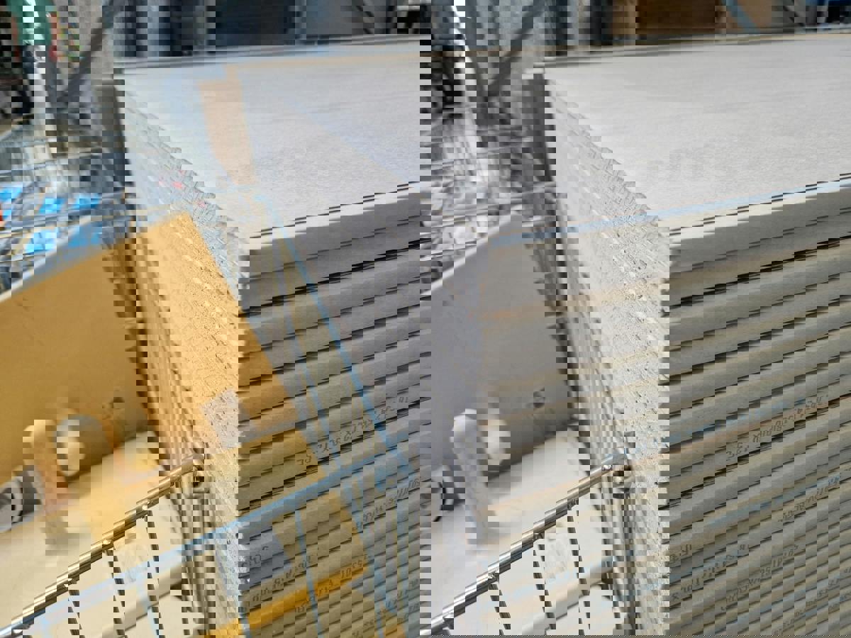 Närbild på stapel med gipsskivor i bygghandel, och intill syns även några gula handverktyg för plattsättning liggandes i ett metallställ för plattsättning.