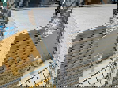 logo Närbild på stapel med gipsskivor i bygghandel, och intill syns även några gula handverktyg för plattsättning liggandes i ett metallställ för plattsättning.
