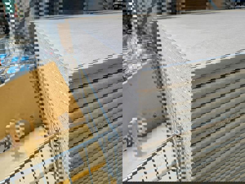 Närbild på stapel med gipsskivor i bygghandel, och intill syns även några gula handverktyg för plattsättning liggandes i ett metallställ för plattsättning.