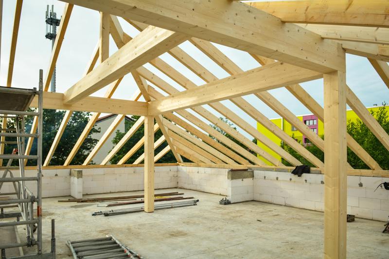 Pågående husbygge med nyinstallerade takstolar i trä ovanpå väggar av lättbetong, med byggställning och material på golvet.