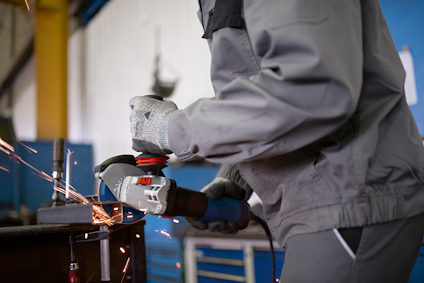 Person slipar metall med vinkelslip i verkstad, gnistor flyger.