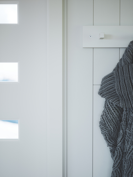 Vit dörr med små glasrutor och en vägg i samma nyans. En grå kappa hänger på en krok.