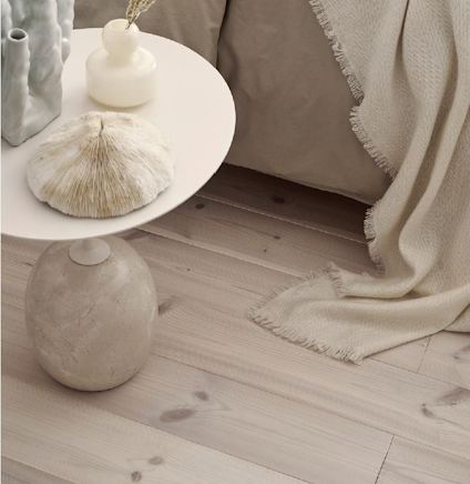 Runt bord med dekorativa vaser och snäckskal, stående på ett ljust trägolv bredvid en soffa med en beige filt.