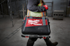 Person bär Milwaukee Packout-väska med rött och svart mönster.