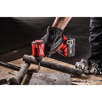 En person borrar i betong med en röd och svart sladdlös borrmaskin. Handen bär en arbetshandske.