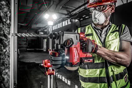 Person i reflexväst och hjälm använder en elektrisk borrmaskin mot en betongvägg.