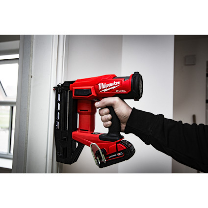 En röd Milwaukee FUEL spikpistol som håller på att användas mot en dörrkarm.