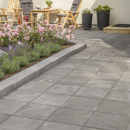 Stenyta med trädgårdsmöbler och rosa blommor intill, omgiven av krukväxter.