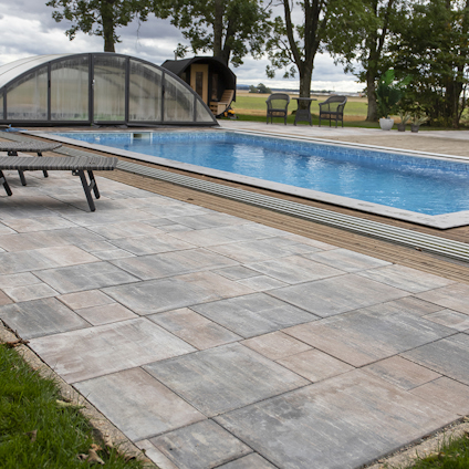 Utomhuspool med genomskinligt skjutbart tak, stenbelagd yta och sittmöbler i bakgrunden.