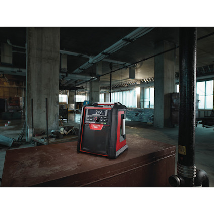 Radio med digital display som visar texten "9:42", placerad på en stor låda i en industriell miljö.