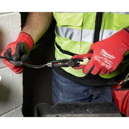 Person i reflexväst och röda handskar arbetar med tång och kabel.
