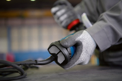 En person i arbetshandskar håller i en elkabel och ett verktyg.