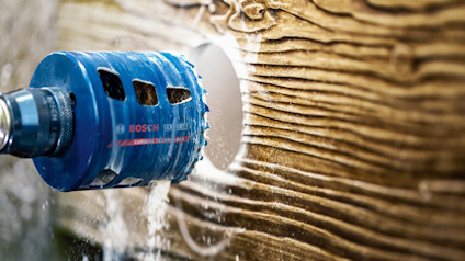Hålsåg borrar ett cirkulärt hål i trä med synliga träspån och Bosch-logotyp på sågen.