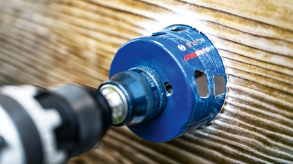 Borrmaskin med blå sågkrona borrar i träyta.