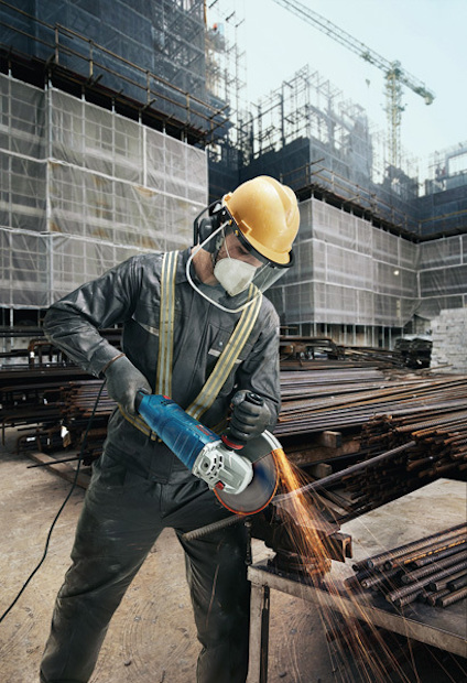 Byggnadsarbetare i hjälm och skyddsmask använder vinkelslip vid byggarbetsplats.