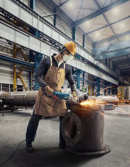 Person som slipar en stor metallventil i en industriverkstad, med gnistor flygande från slipmaskinen.
