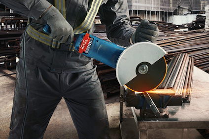 Person i arbetskläder använder vinkelslip för att skära metalldelar i en verkstadsmiljö.