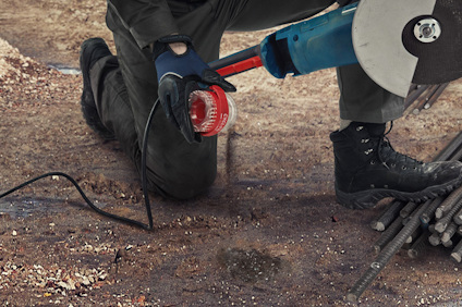 Person använder vinkelslip för att skära metallstänger på marken.