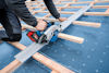 En person använder en cirkelsåg för att såga ett träreglar över en blå presenning med korsmönster.