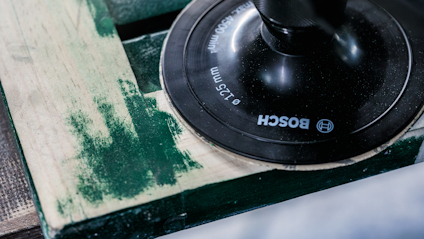 Slipmaskin från Bosch med rund slippyta på en grön träyta. Text på maskinen: "BOSCH Ø125 mm".