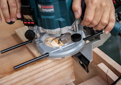En person använder en handöverfräs för att bearbeta trä, med märke "Bosch Professional" synligt på verktyget.