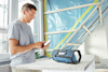 Man in a t-shirt using a smartphone next to a portable radio on a wooden workbench in a partially constructed room.