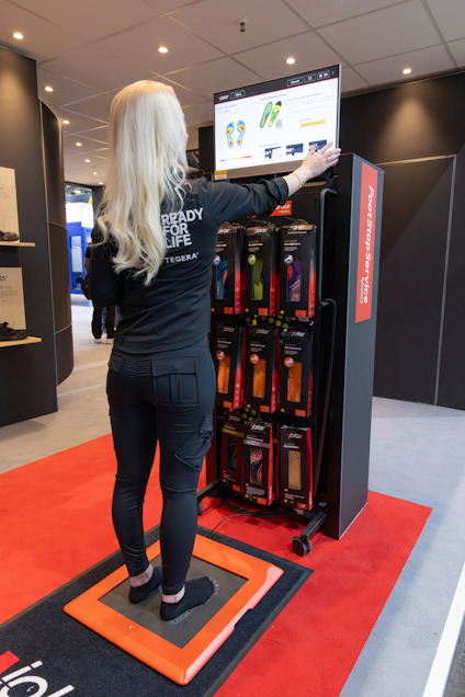 Kvinna står på en digital scanner framför en skärm som visar skoinläggsinformation.