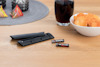 Fjärrkontrollens batterilucka och batterier på bord, bredvid skål med chips och glas med dryck.